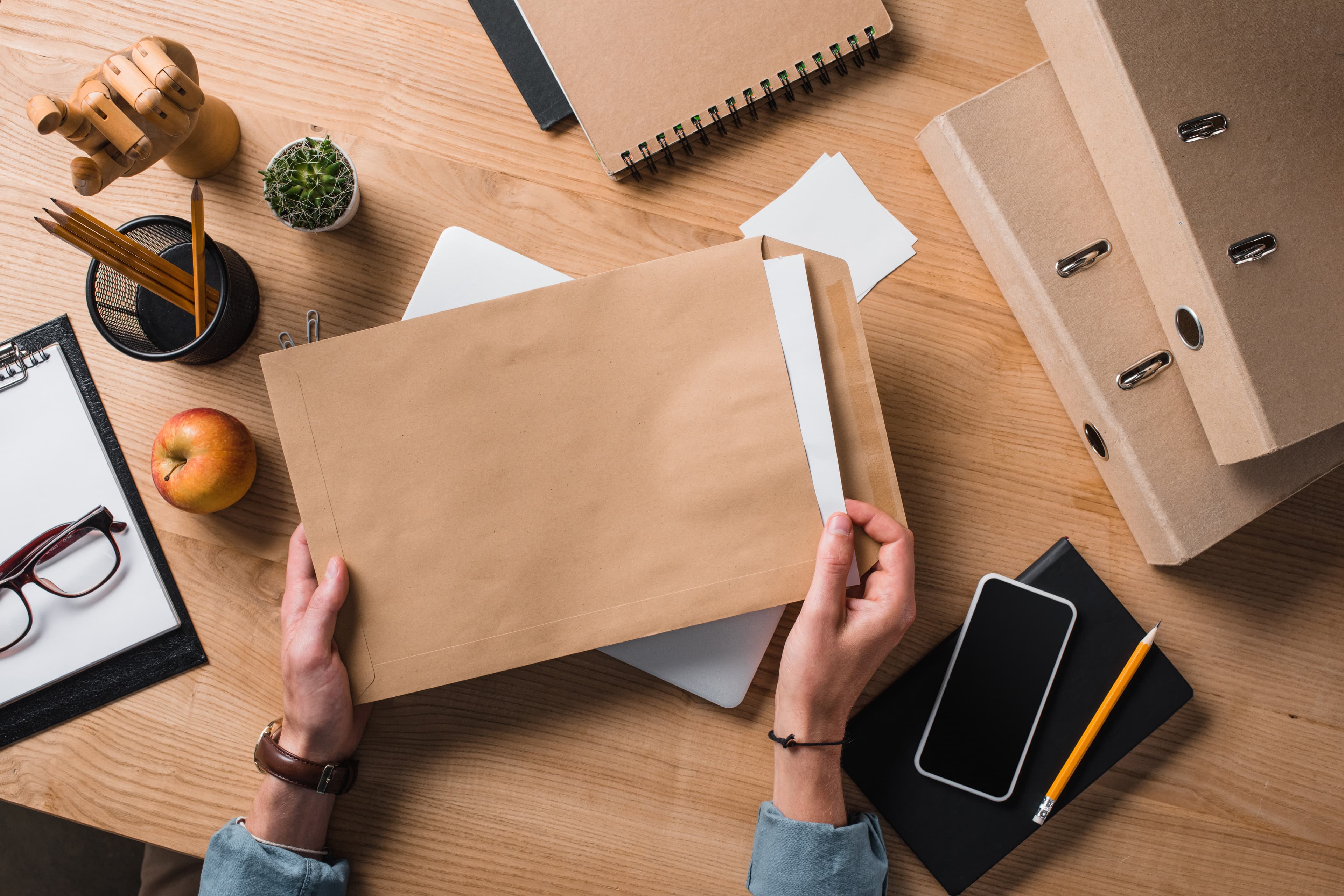 Hands holding a manila document envelope on a wooden desk
